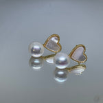 Heart-shaped white fritillaria and freshwater pearl stud earrings are reflected on a surface.
