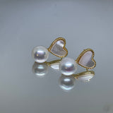 Heart-shaped white fritillaria and freshwater pearl stud earrings are reflected on a surface.