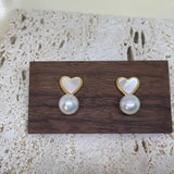 Two heart-shaped white fritillaria and freshwater pearl stud earrings on a wooden block.