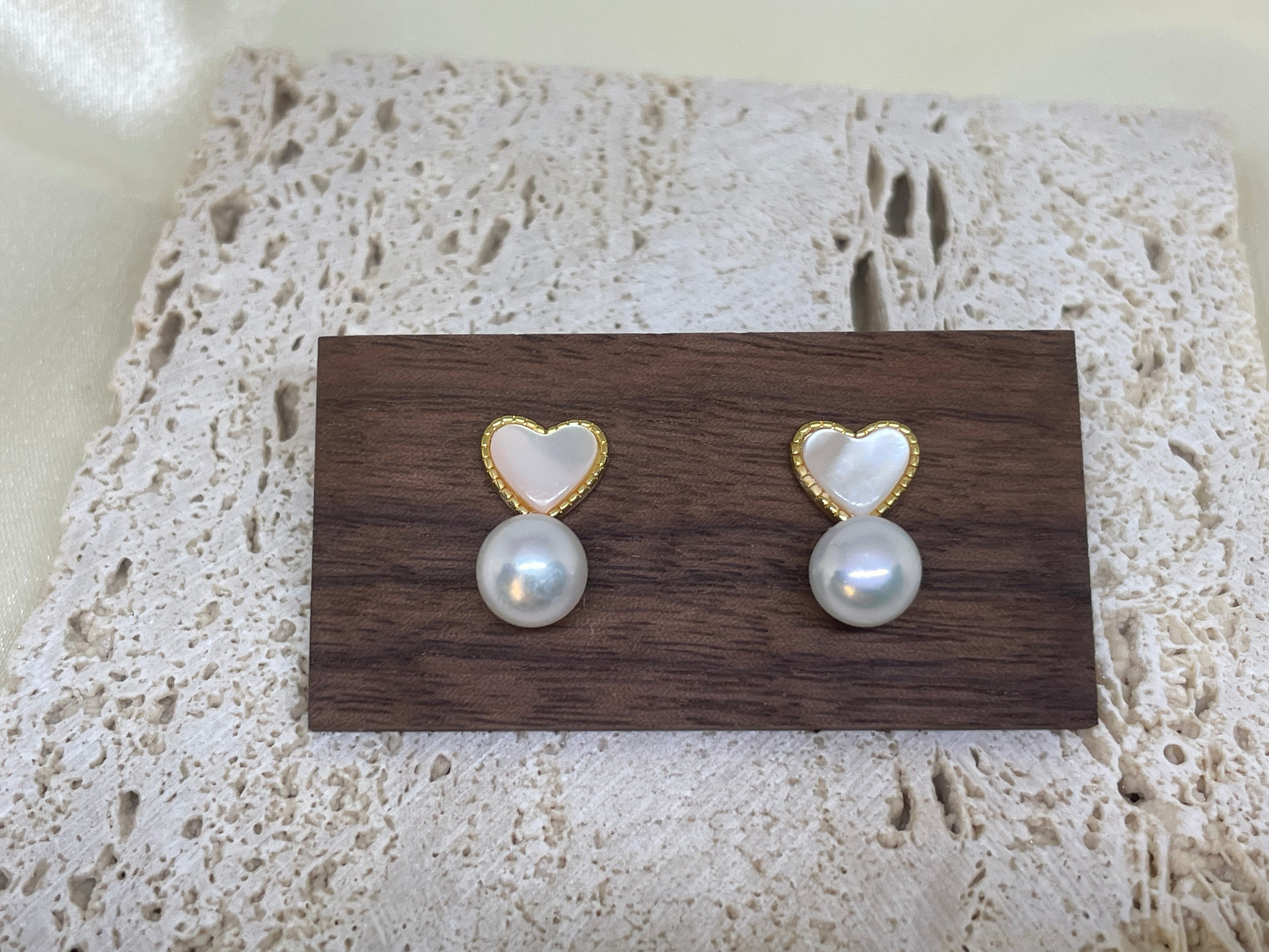 Two heart-shaped white fritillaria and freshwater pearl stud earrings on a wooden block.