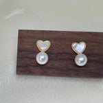 Heart-shaped white fritillaria and freshwater pearl stud earrings on a wooden block.