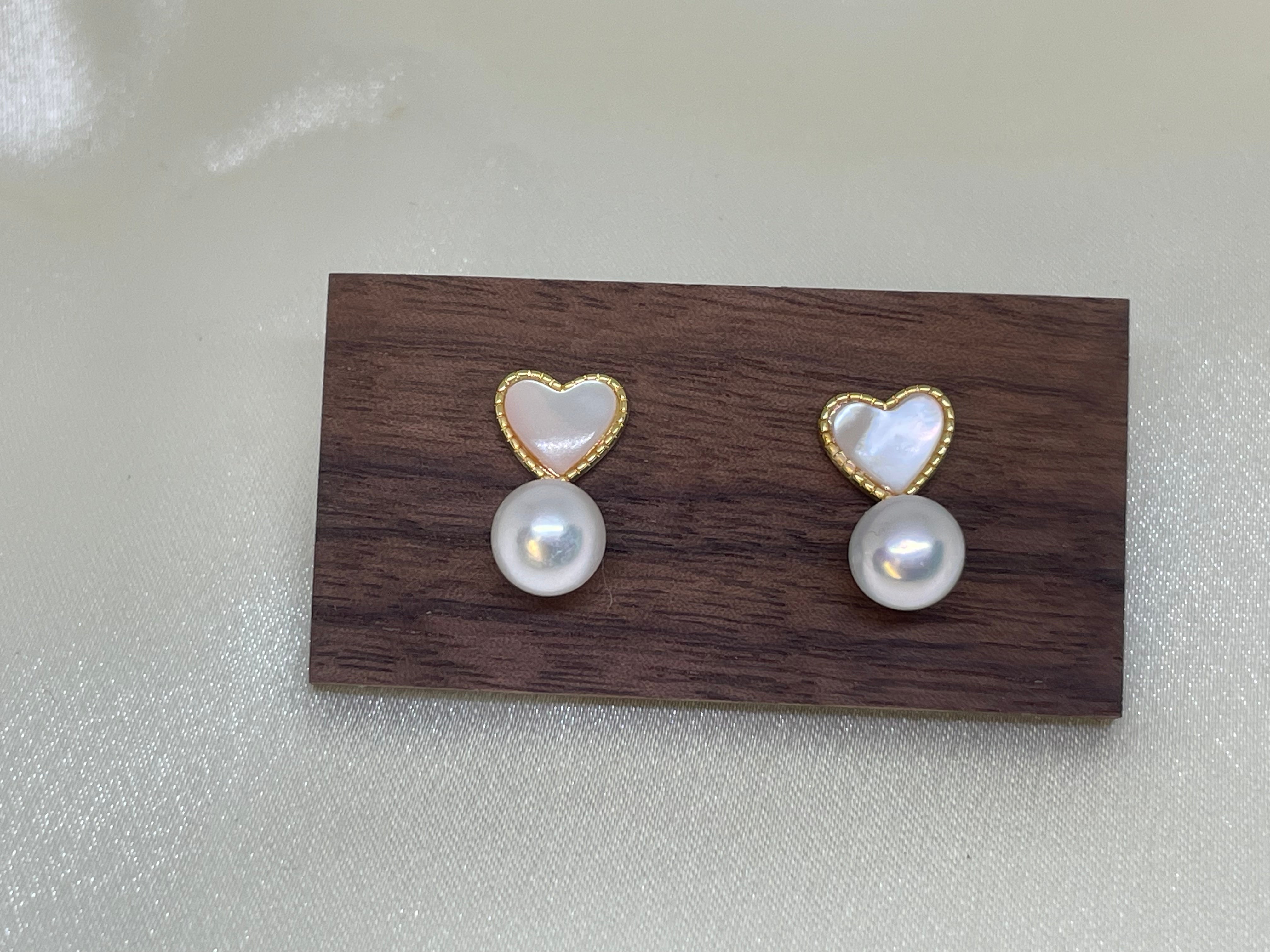 Heart-shaped white fritillaria and freshwater pearl stud earrings on a wooden block.