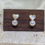 Heart-shaped white fritillaria and freshwater pearl stud earrings on a wooden display.