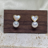 Heart-shaped white fritillaria and freshwater pearl stud earrings on a wooden display.