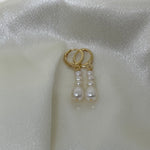 Elegant multi-pearl dangle earrings with gold-toned hoops on a white satin background.