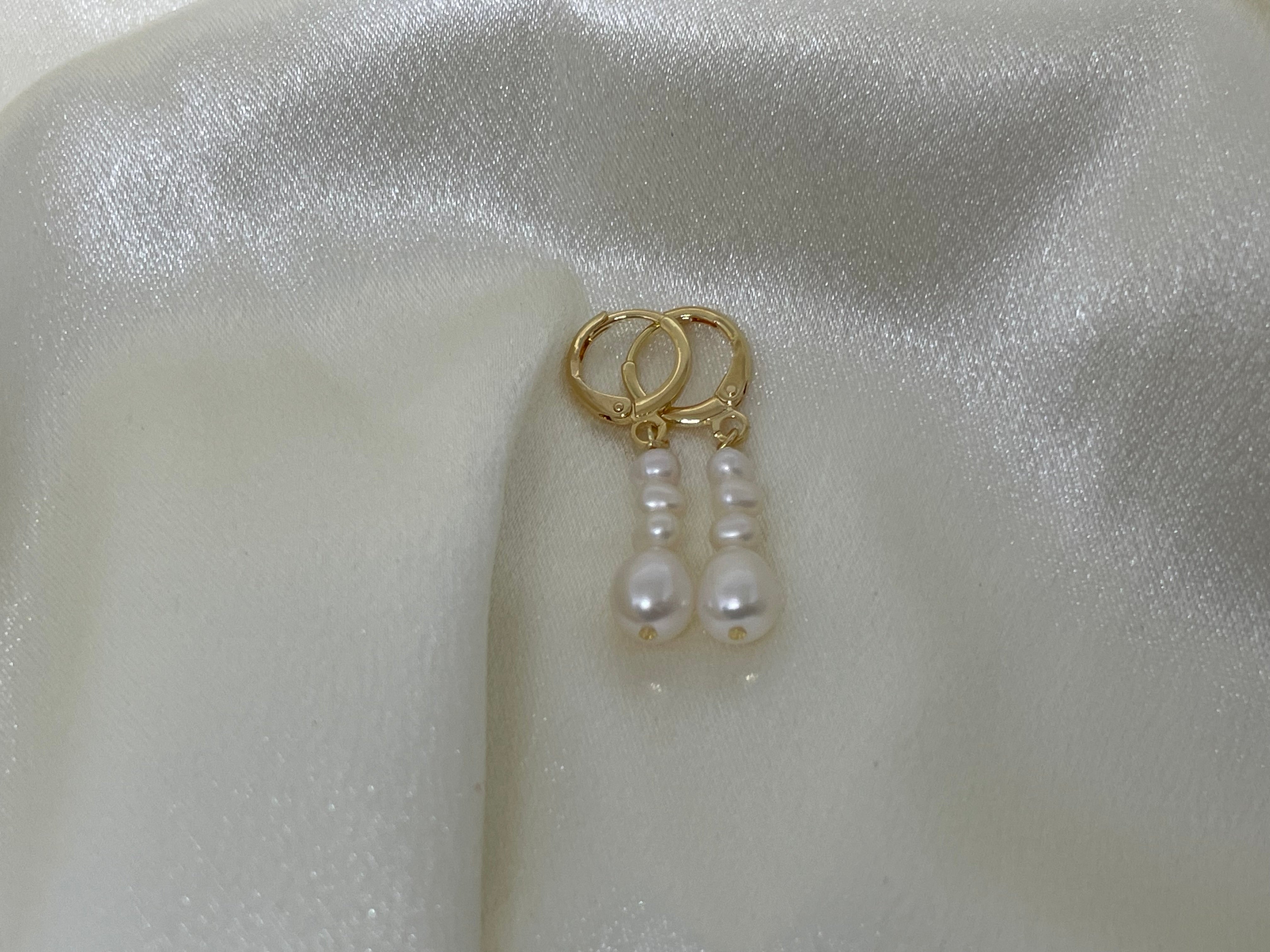 Elegant multi-pearl dangle earrings with gold-toned hoops on a white satin background.