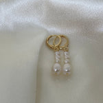 Gold hoop earrings with three dangling white pearls on a white satin background.