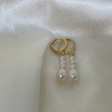 Gold hoop earrings with three dangling white pearls on a white satin background.