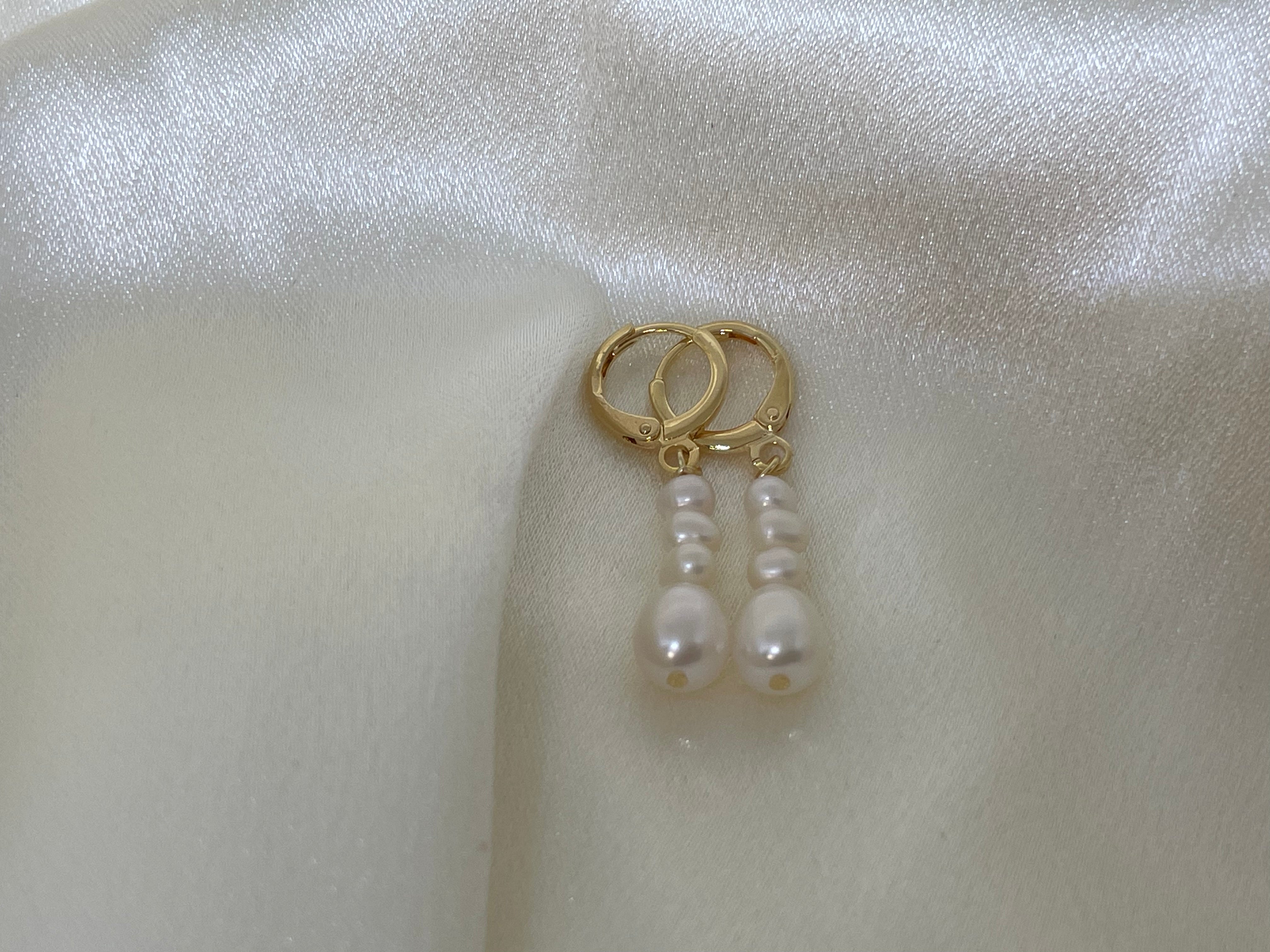 Gold hoop earrings with three dangling white pearls on a white satin background.