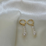 Elegant multi-pearl dangle earrings with gold-tone hoops on a white satin background.