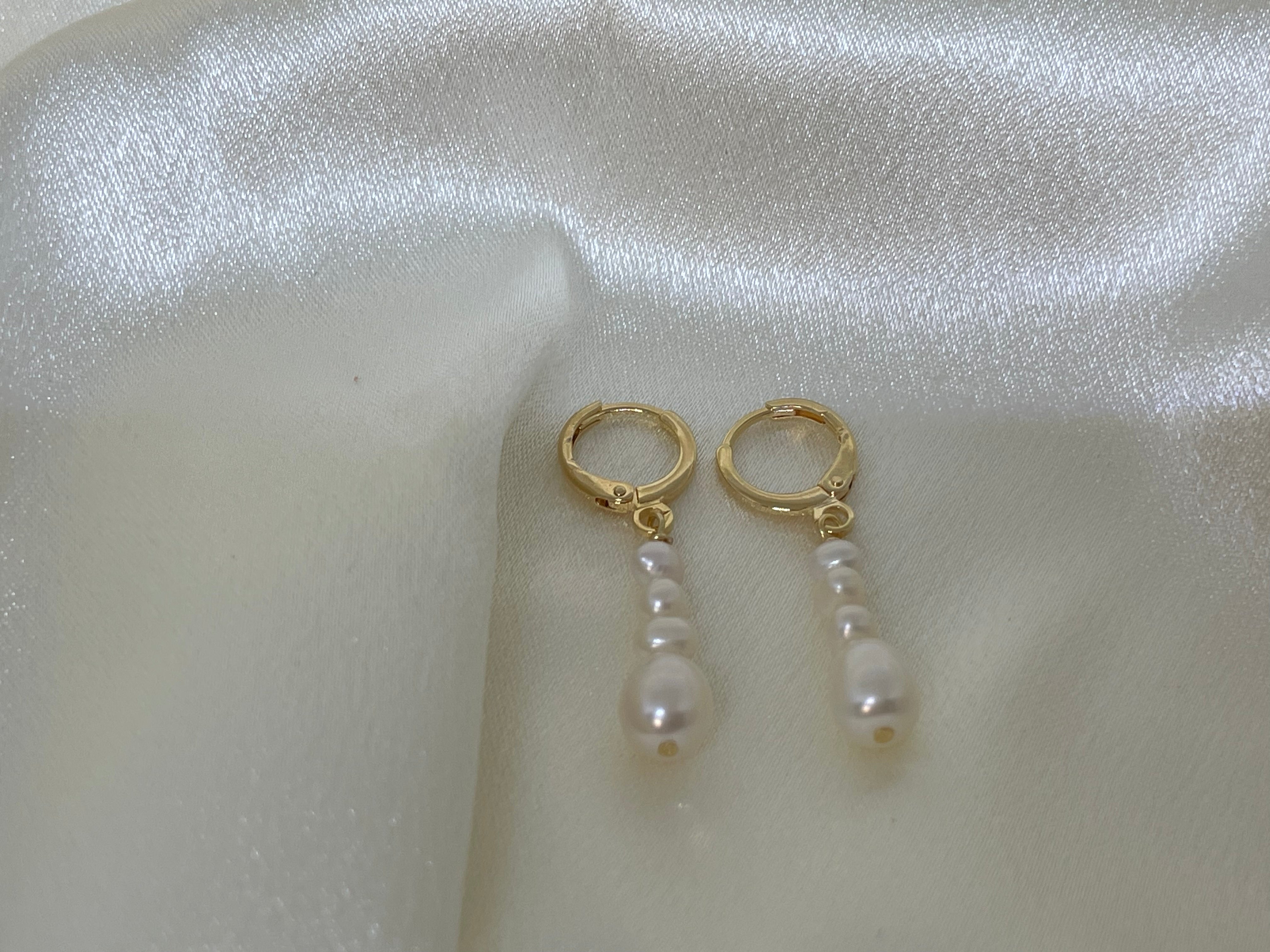 Elegant multi-pearl dangle earrings with gold-tone hoops on a white satin background.