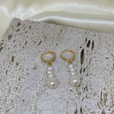 Two gold hoop earrings with three dangling white pearls each, on a textured white surface.