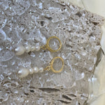 Two gold hoop earrings with dangling multi-pearl chains rest on a textured surface.