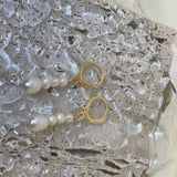 Two gold hoop earrings with dangling multi-pearl chains rest on a textured surface.