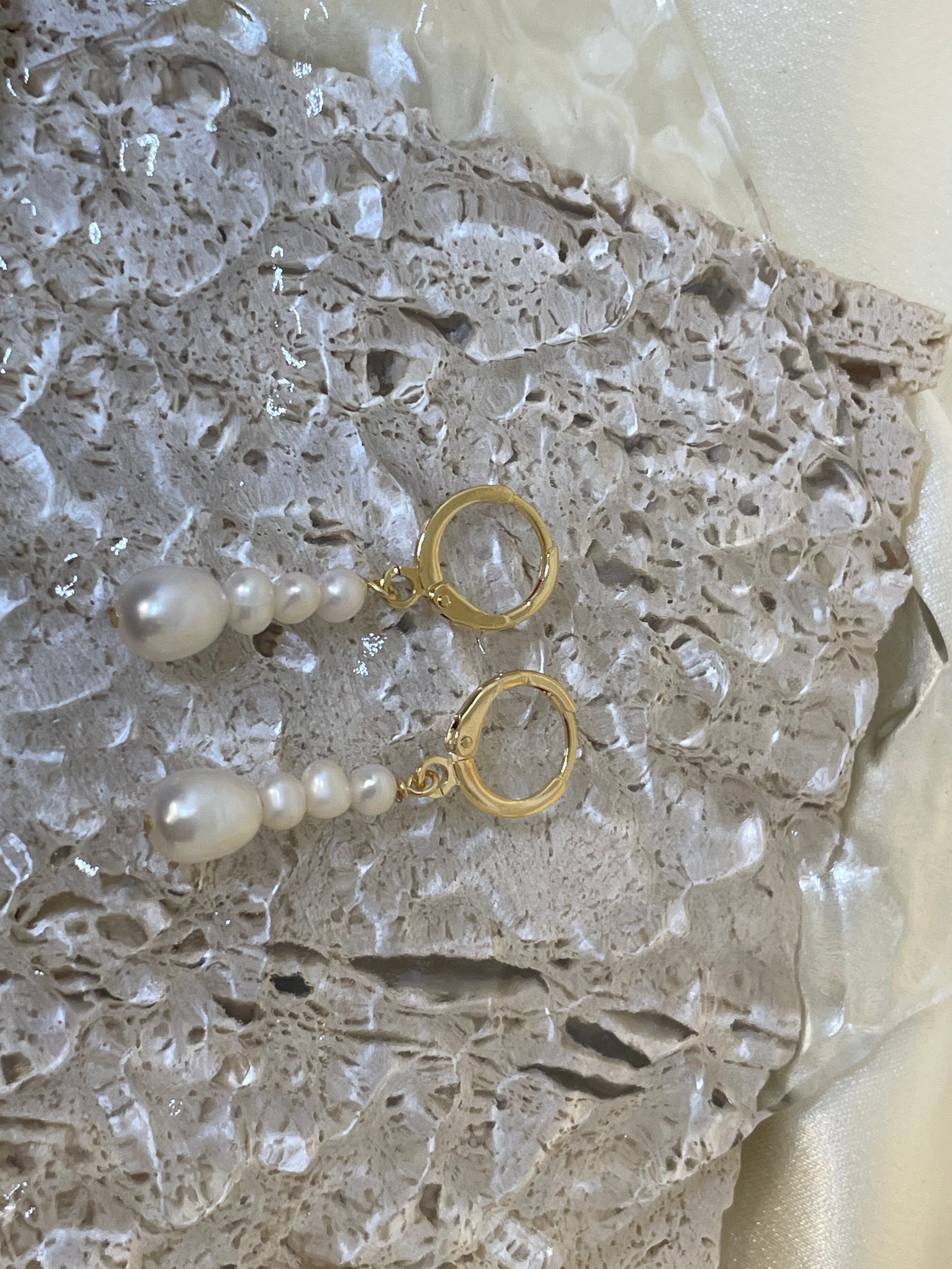 Two gold hoop earrings with dangling multi-pearl chains rest on a textured surface.