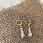 Elegant gold hoop earrings with dangling white pearls on a burlap background.