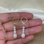 Elegant multi-pearl dangle earrings held in a hand against a light background.
