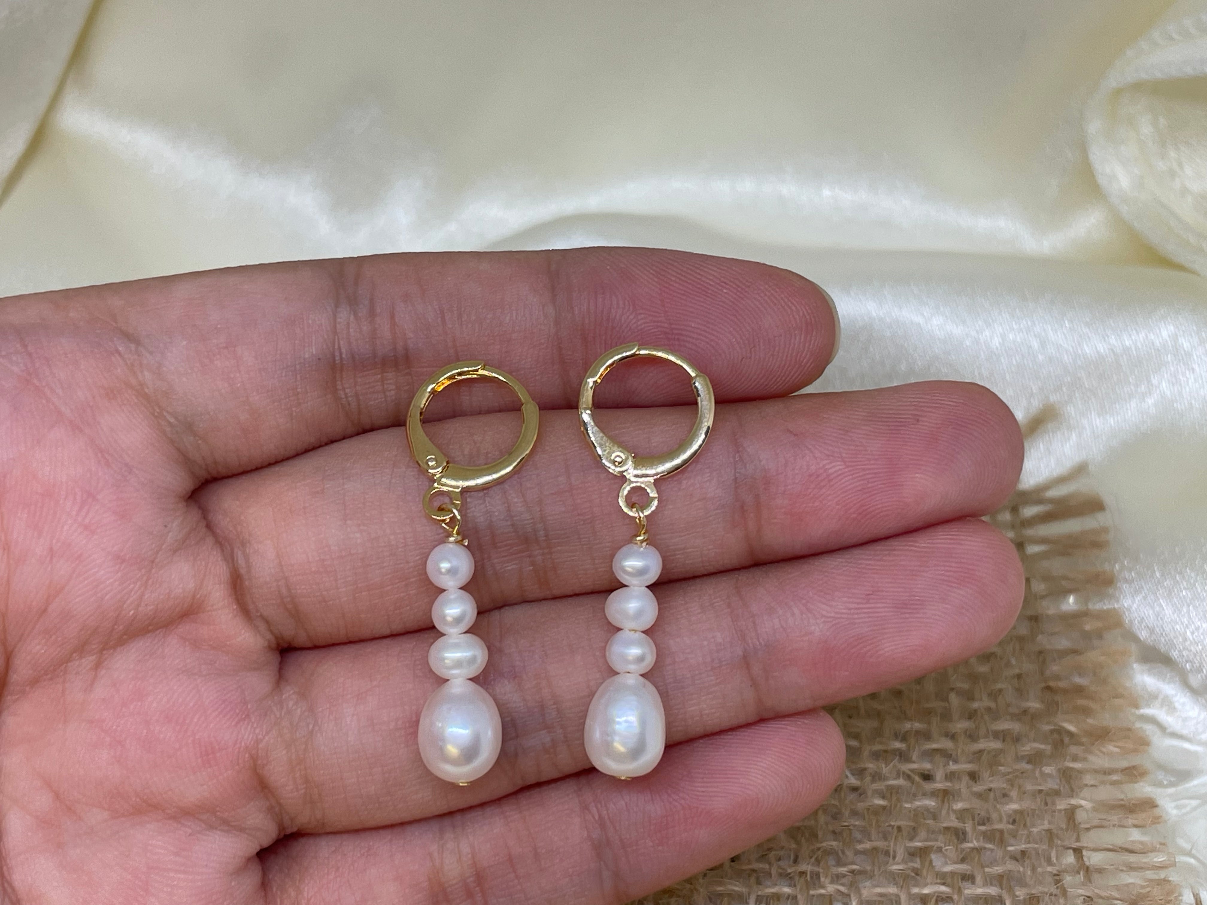 Elegant multi-pearl dangle earrings held in a hand against a light background.