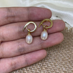 Two gold twist earrings with dangling freshwater pearls are held in a hand.