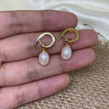 Two gold twist earrings with dangling freshwater pearls are held in a hand.
