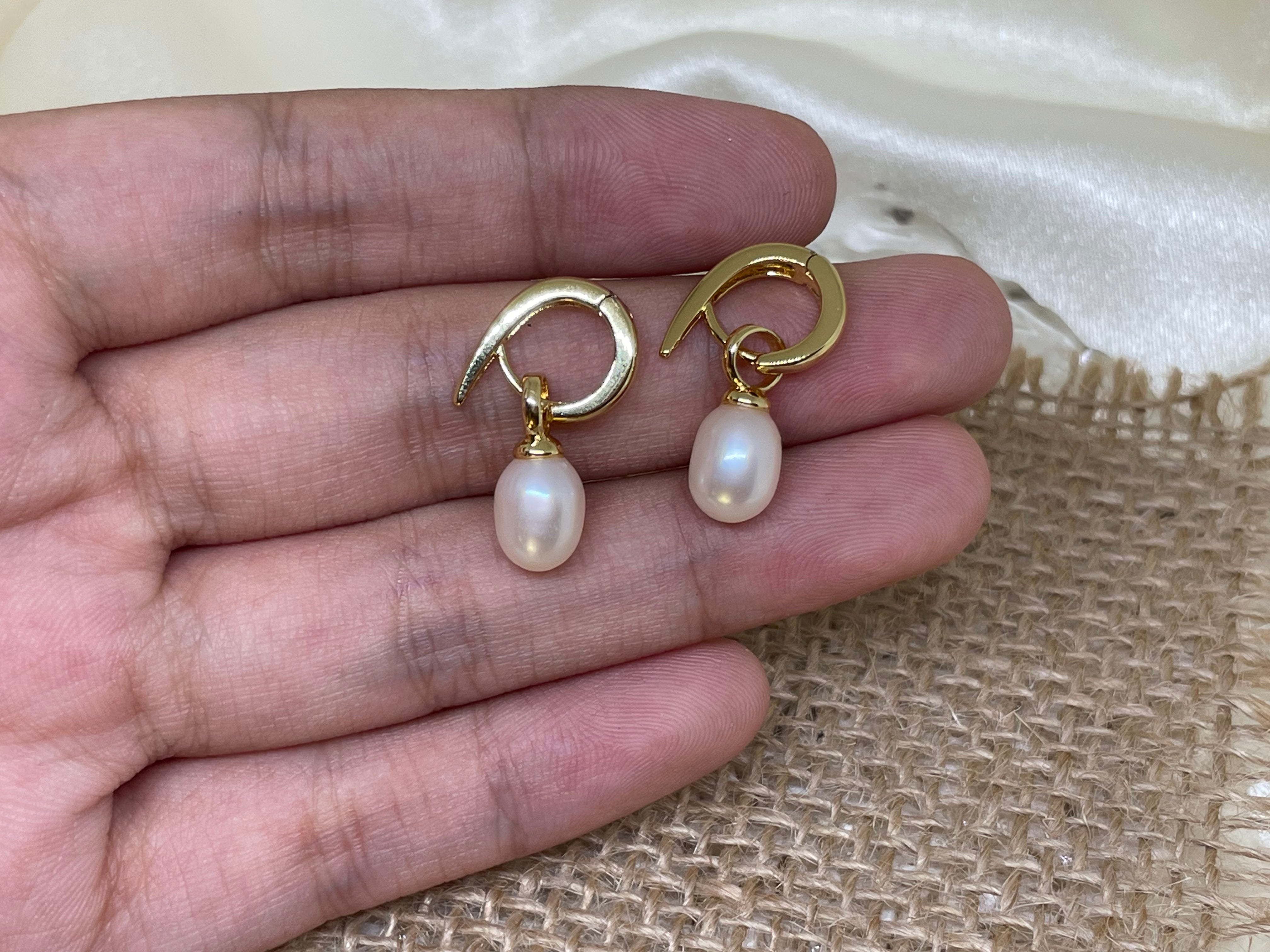 Two gold twist earrings with dangling freshwater pearls are held in a hand.