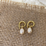 Two gold twist earrings with freshwater pearls are displayed on a burlap surface.
