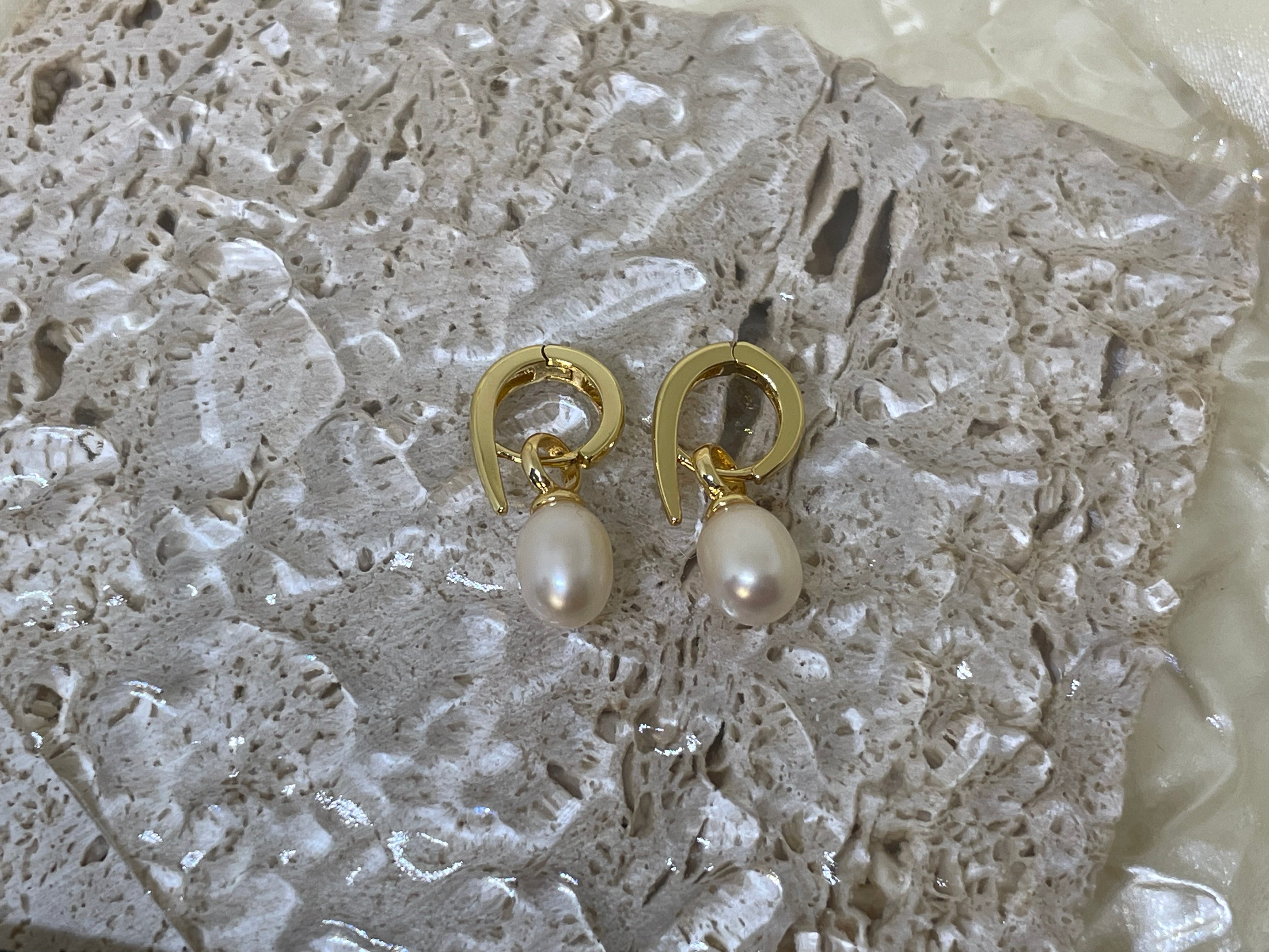 A pair of gold twist earrings with dangling freshwater pearls rests on a textured surface.