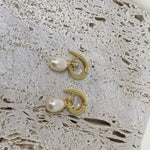 Two gold twist earrings with freshwater pearls are displayed on a textured surface.
