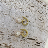 Two gold twist earrings with freshwater pearls are displayed on a textured surface.
