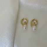 Two gold twist earrings with freshwater pearl drops are displayed on a white, shimmery fabric.