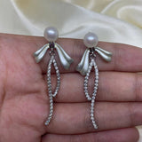 Elegant pearl bow dangle earrings with a silver-plated chain and cubic zirconia.