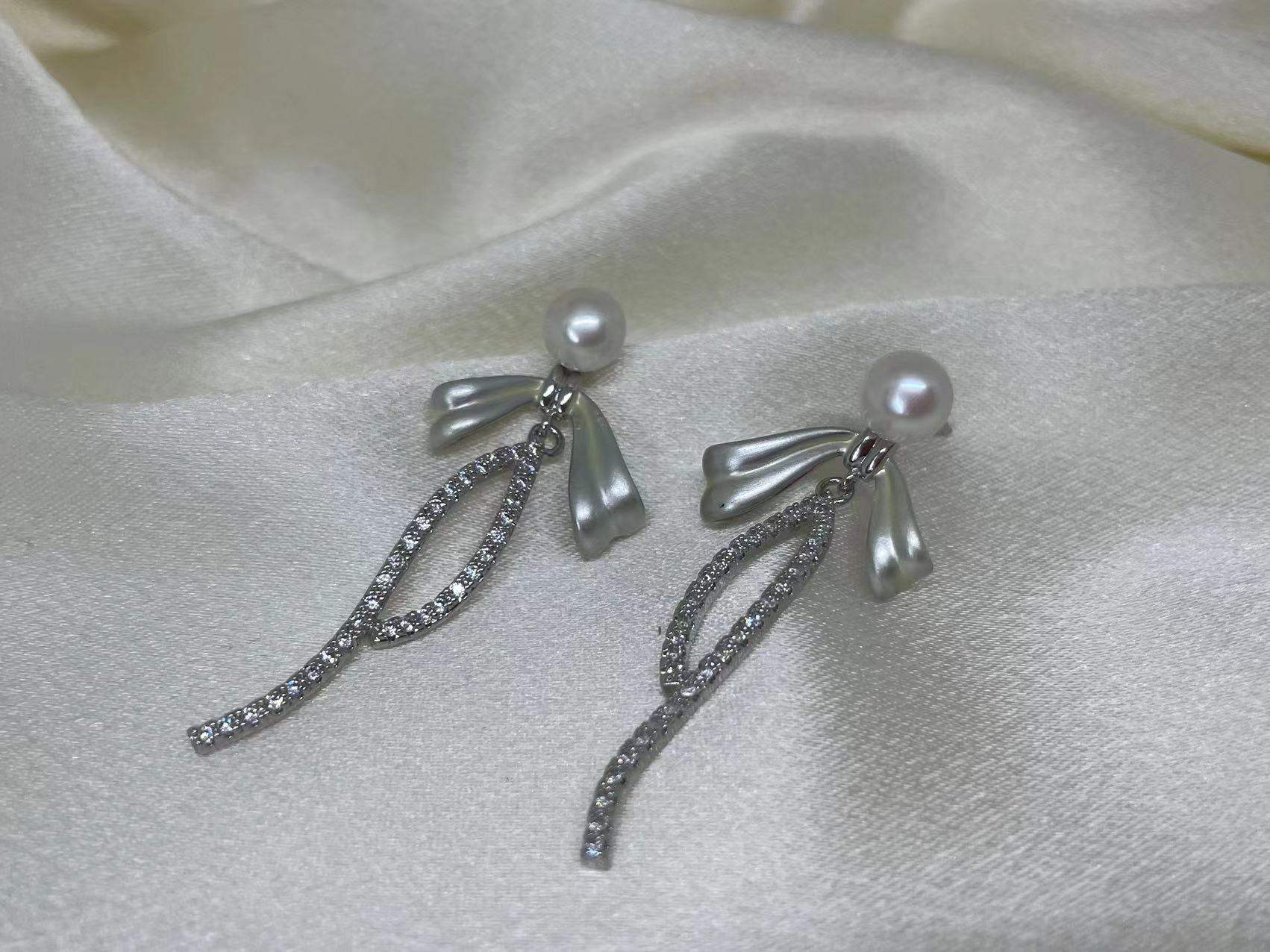 Elegant pearl bow dangle earrings with a silver-plated chain and cubic zirconia accents.