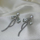 Elegant pearl bow dangle earrings with a silver-plated chain and cubic zirconia accents.