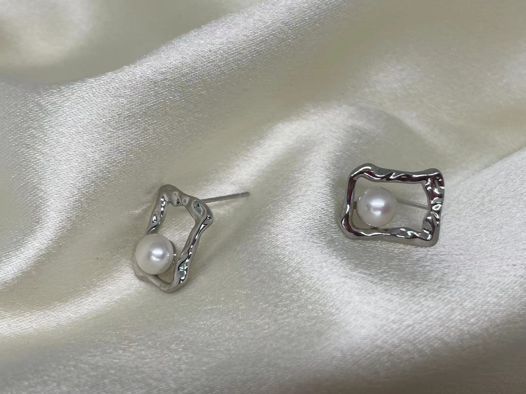 Silver quadrate stud earrings with a freshwater pearl on a white satin background.