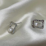 Silver quadrate stud earrings with a freshwater pearl on a white satin background.