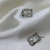 Two silver quadrate stud earrings with freshwater pearls are displayed on white silk.