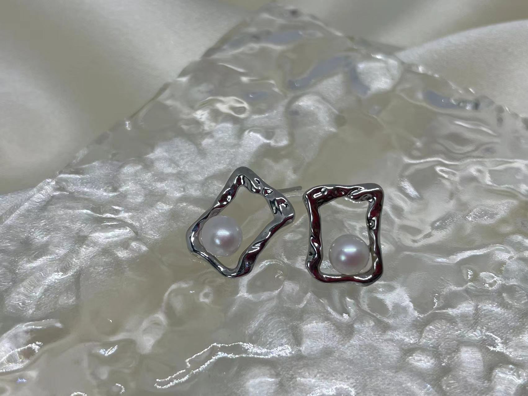 Two silver-toned, irregularly shaped square stud earrings with a single pearl in each.