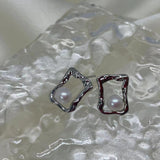 Two silver-toned, irregularly shaped square stud earrings with a single pearl in each.