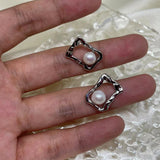 Two silver quadrate stud earrings with freshwater pearls are held in a hand.