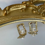Gold quadrate stud earrings with freshwater pearls, displayed on a mirrored surface.