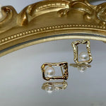 Gold quadrate stud earrings with a freshwater pearl, displayed on a mirrored surface.