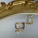 Gold quadrate stud earrings with a freshwater pearl, displayed on a mirrored surface.