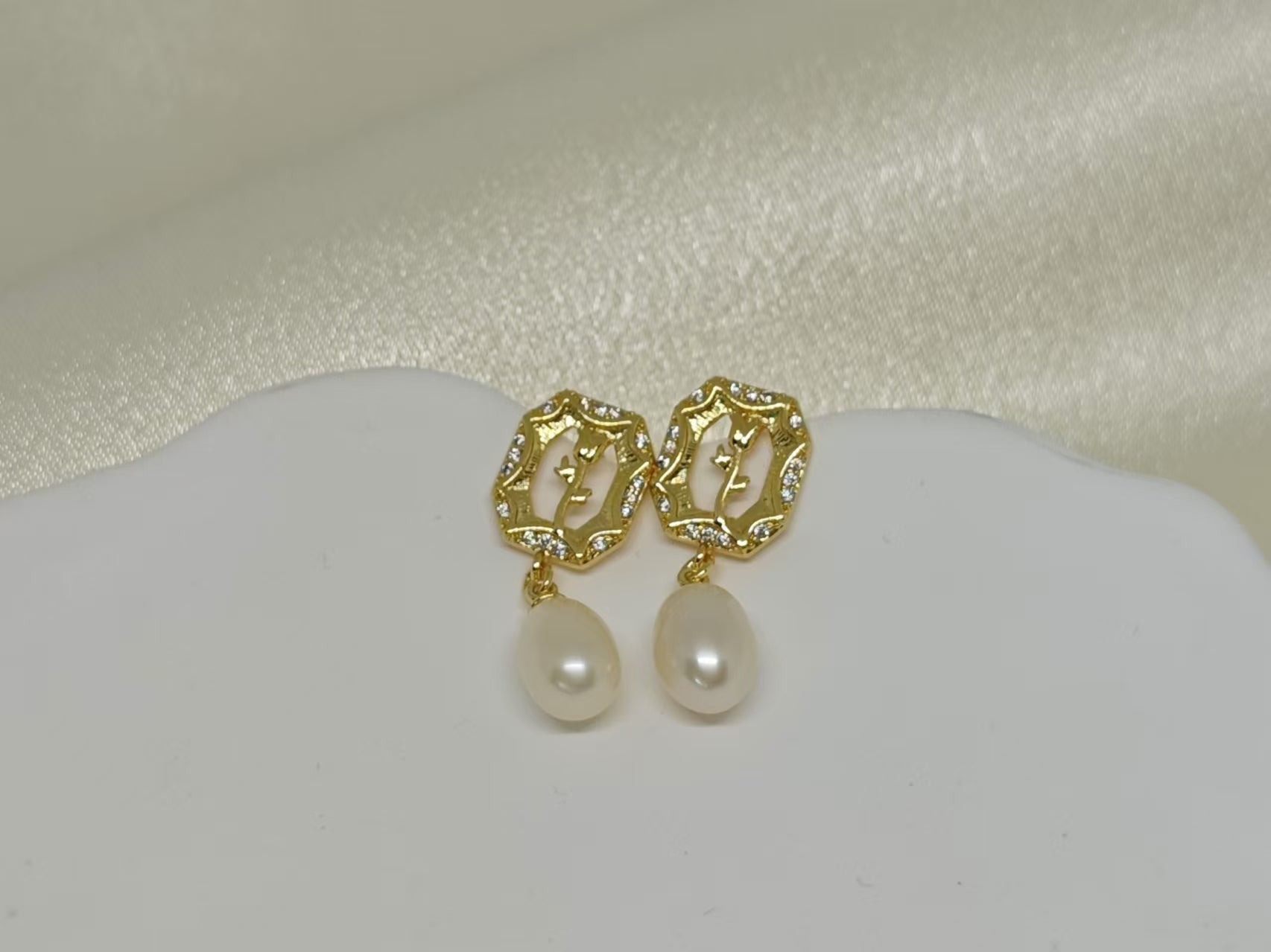 Gold-plated earrings with a rose design, clear stones, and dangling freshwater pearls.
