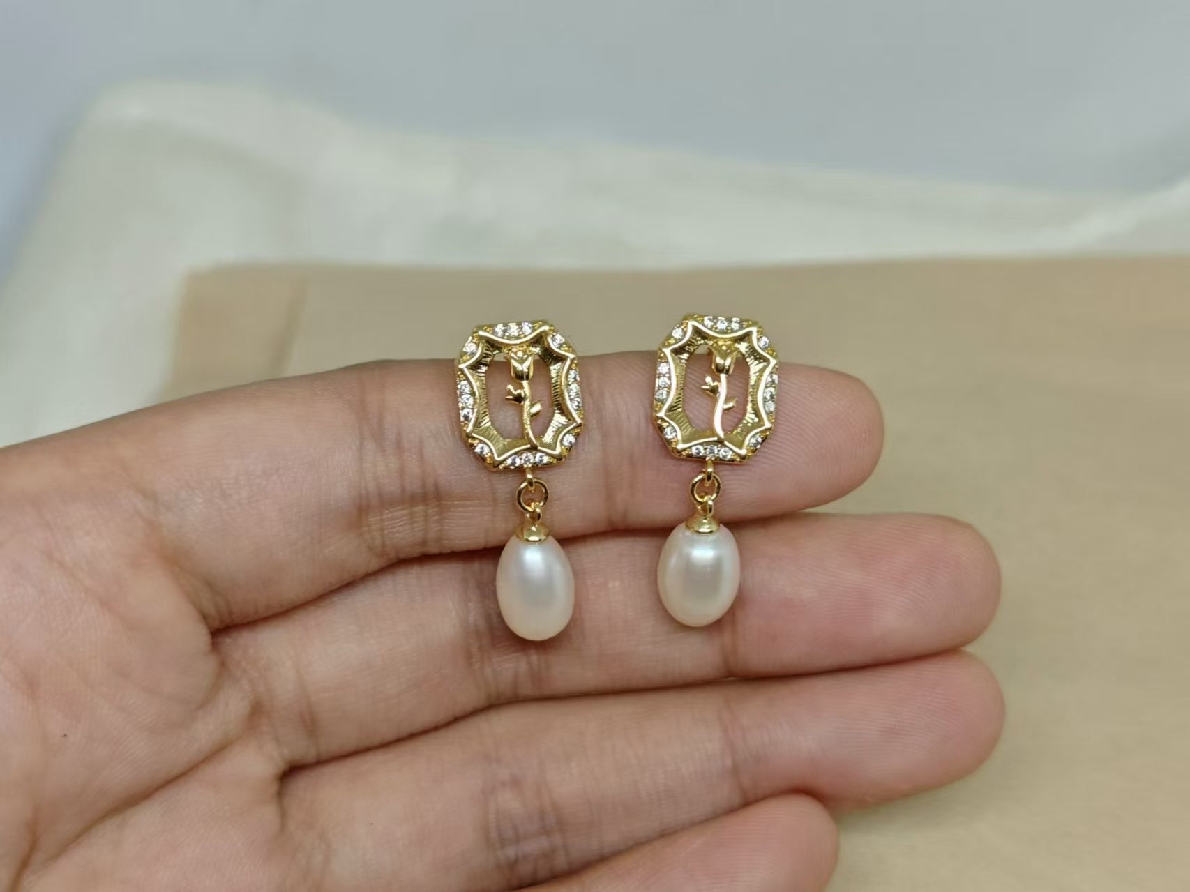 Gold-plated earrings with a rose design, surrounded by small gems, and a dangling pearl.