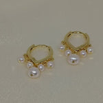 Two gold hoop earrings each adorned with five freshwater pearls.
