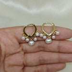 Two gold hoop earrings, each with five dangling freshwater pearls, are held in a hand.