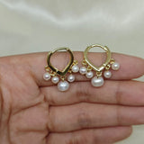 Two gold hoop earrings, each with five dangling freshwater pearls, are held in a hand.