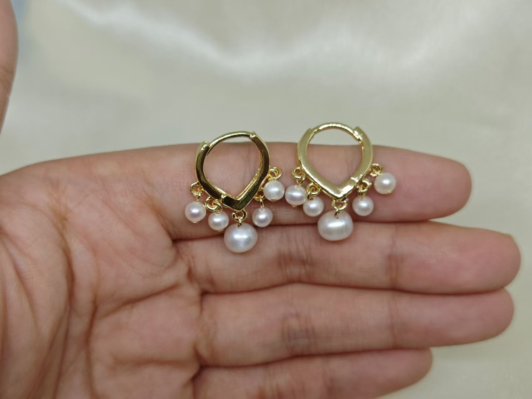 Two gold hoop earrings, each with five dangling freshwater pearls, are held in a hand.
