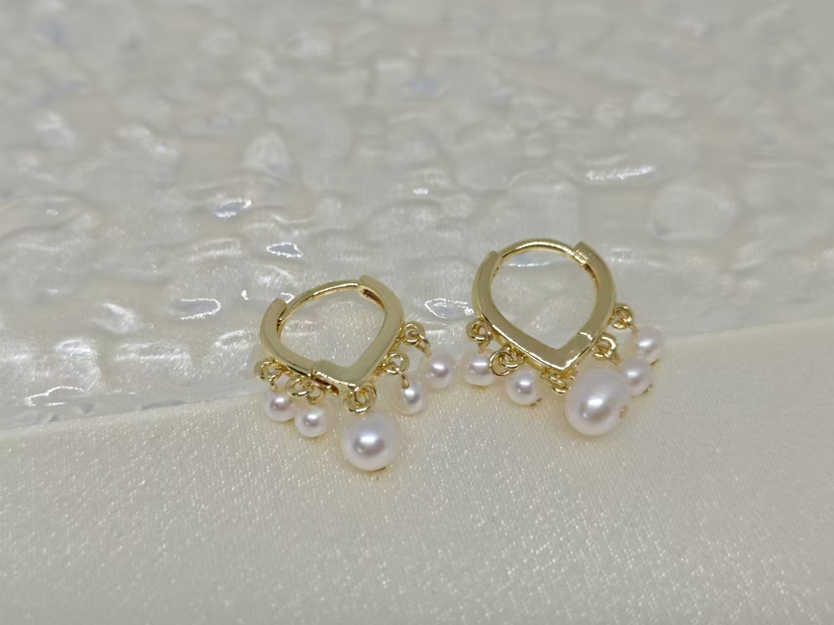 Two gold hoop earrings with five freshwater pearls each are displayed on a white surface.