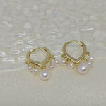 Two gold hoop earrings with five freshwater pearls each are displayed on a white surface.